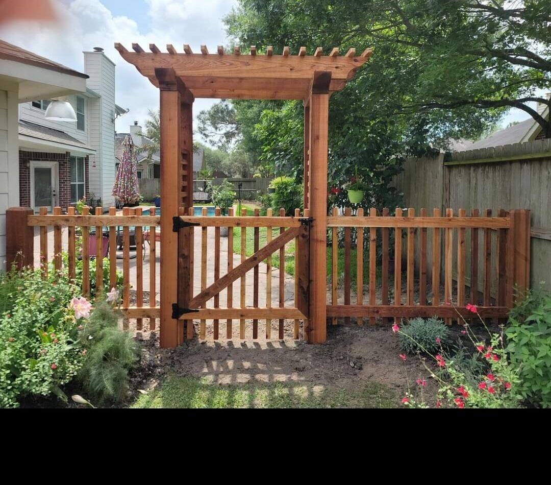 Wood arbor and gate with picket fence and flower bed