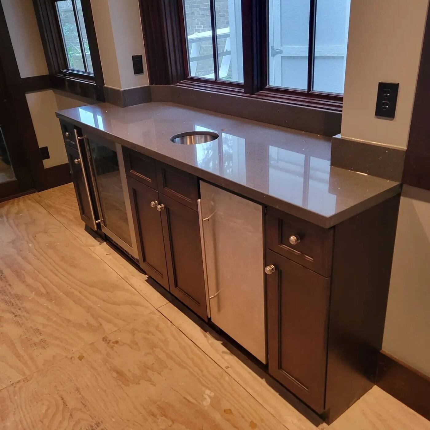 Dark wet bar cabinetry with stone counter under windows